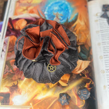 Load image into Gallery viewer, A grey and orange dice bag is closed on a gaming table with a dice tray and D&D books in the background.