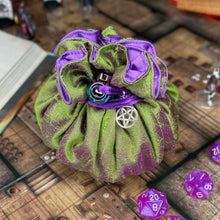 Load image into Gallery viewer, A green and purple dice bag with a pentagram charm sits closed on a D&D map.