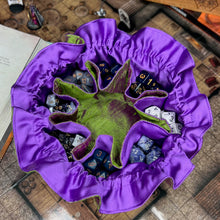 Load image into Gallery viewer, A green and purple dice bag sits open on top of D&D maps. Inside, the pockets are filled with colorful dice.