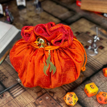 Load image into Gallery viewer, A bright orange and red dice bag with a gold fire emblem charm sits closed on a D&D map.