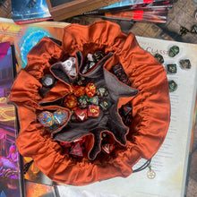 Load image into Gallery viewer, A grey and orange dice bag is opened on a gaming table with a dice tray and D&D books in the background.