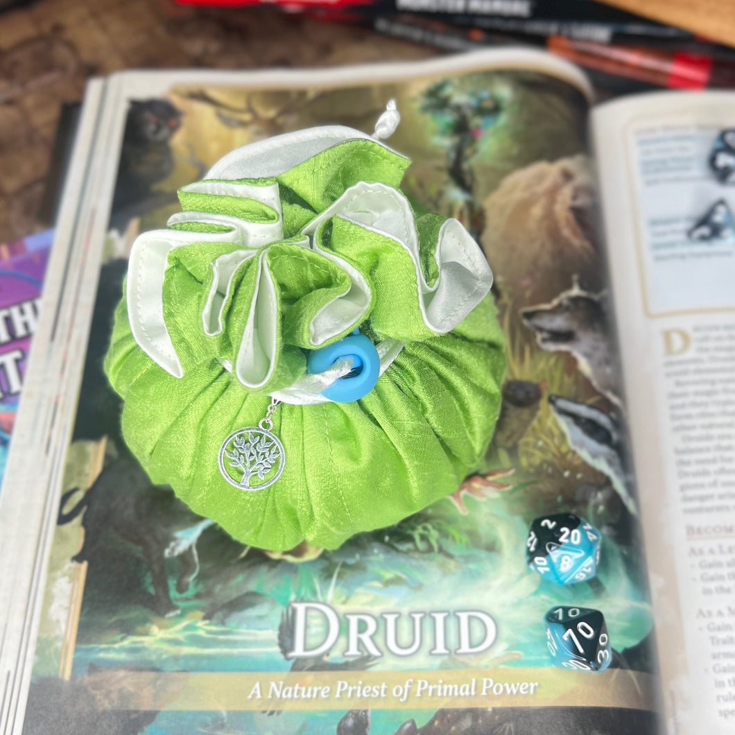 A green and white dice bag is closed on a gaming table with a dice tray and D&D books in the background.