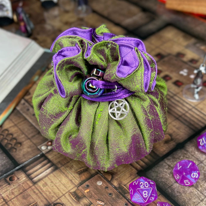 A green and purple dice bag with a pentagram charm sits closed on a D&D map.