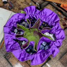 Load image into Gallery viewer, A green and purple dice bag sits open on top of D&amp;D maps. Inside, the pockets are filled with colorful dice.
