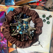 Load image into Gallery viewer, A bronze and brown dice bag is open on a gaming table with a dice tray and D&amp;D books in the background.
