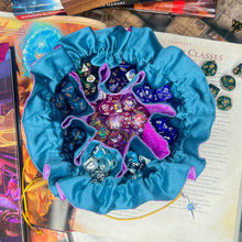 Load image into Gallery viewer, A purple and blue dice bag is open on a gaming table with a dice tray and D&amp;D books in the background.
