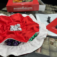 Load image into Gallery viewer, A red dice bag with a white interior is laid out flat on top of a gaming map. You can see colorful dice in the pockets.
