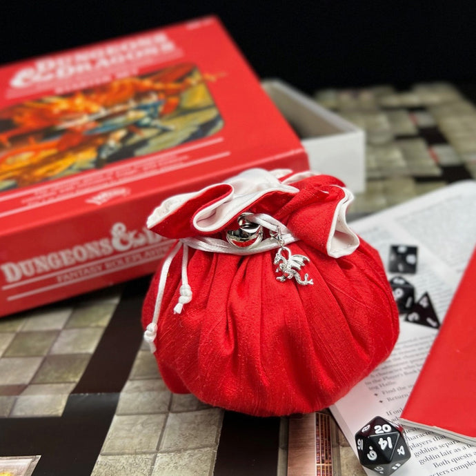 Red dice bag with dragon charm sitting closed in front of the D&D 2nd edition red box