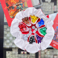 Load image into Gallery viewer, A red dice bag with a white interior sits open on a gaming table. It is full of colorful dice.
