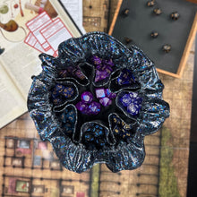 Load image into Gallery viewer, A black and shimmering dice bag sits open on a gaming table. Inside, the pockets are full of colorful dice.
