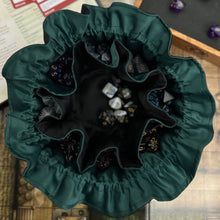 Load image into Gallery viewer, A black and green dice bag sits open on a gaming table. Inside, the pockets are filled with colorful dice.
